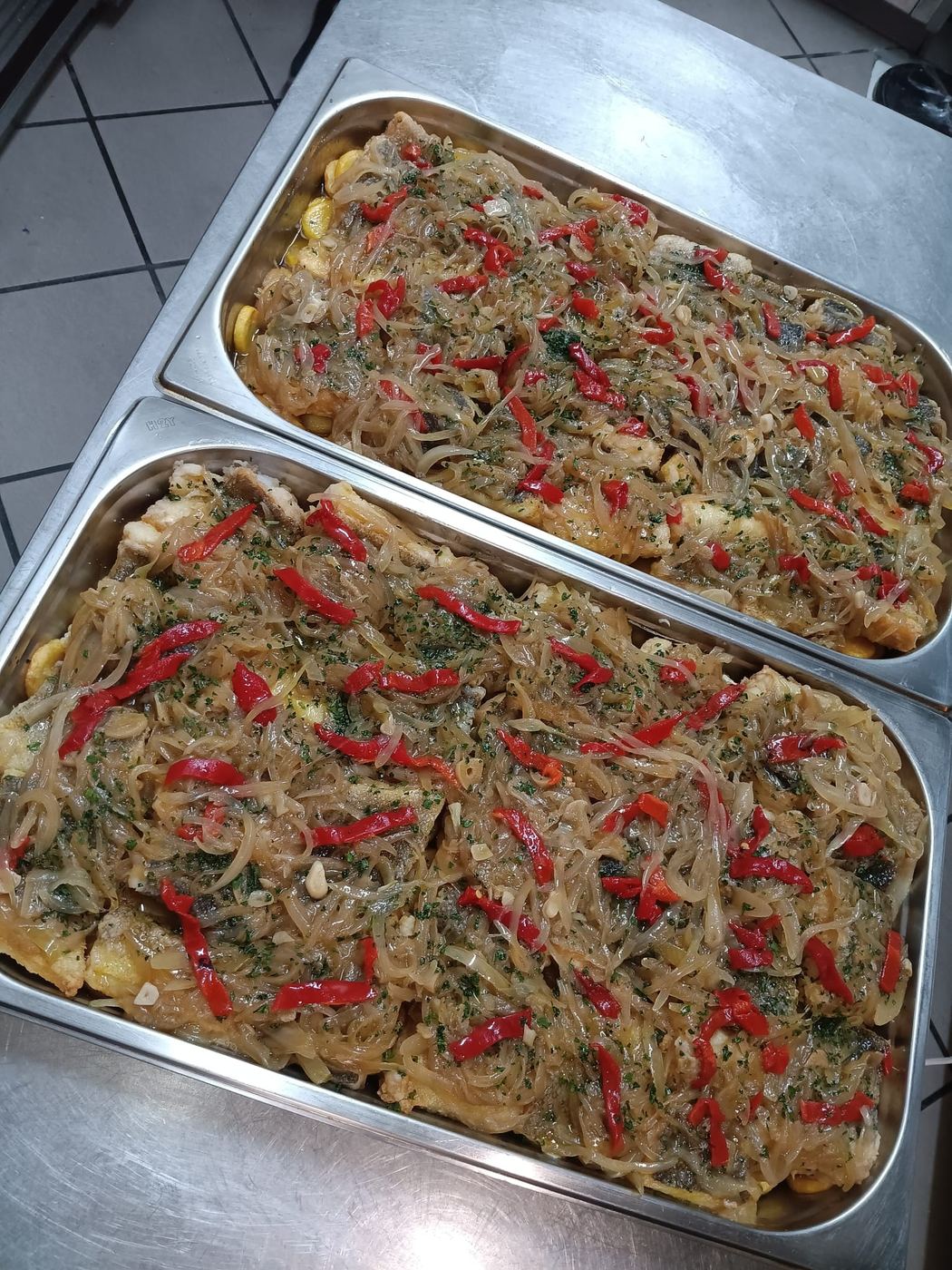 Dois tabuleiros de bacalhau com cebolada e pimento, acabados de sair da cozinha