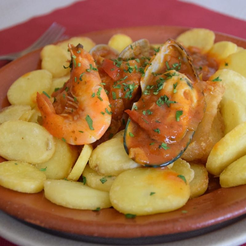 Bacalhau à marinheiro: camarão e mexilhão em molho de tomate sobre batata salteada, num prato de barro