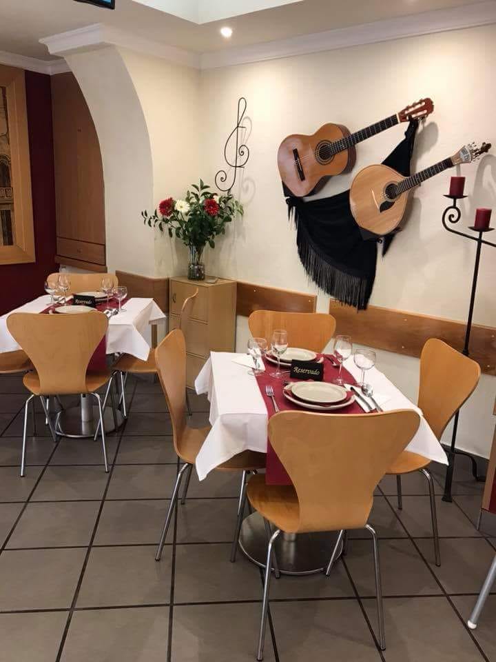 A sala com mesas postas a branco e grená, duas guitarras e um xaile na parede